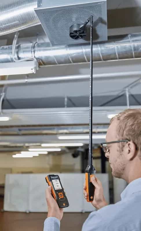 Technik z miernikiem Testo w dłoni używa teleskopu do pomiaru przepływu powietrza w kanale wentylacyjnym pod sufitem (miniatura)