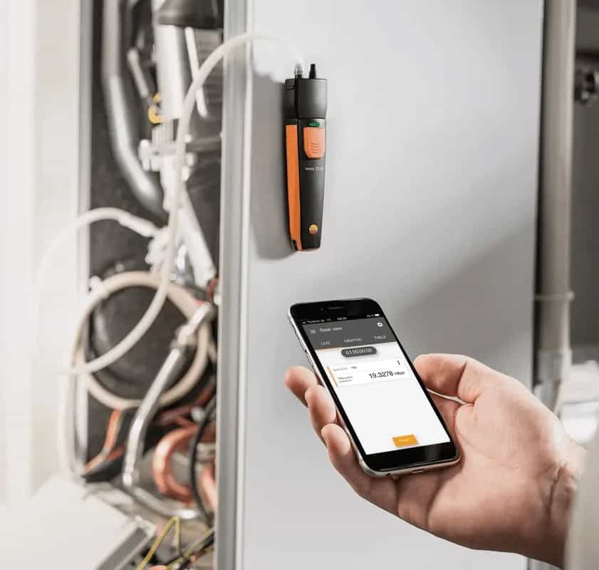 Manometr Testo 510i podpięty do instalacji i odczyt pomiaru w aplikacji na smartfonie trzymanym w dłoni (miniatura)