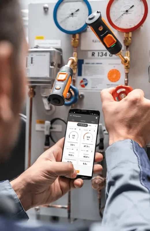Technik odczytuje wyniki pomiaru ciśnienia z aplikacji Testo Smart App na smartfonie przy instalacji chłodniczej z manometrem Testo 549i (miniatura)