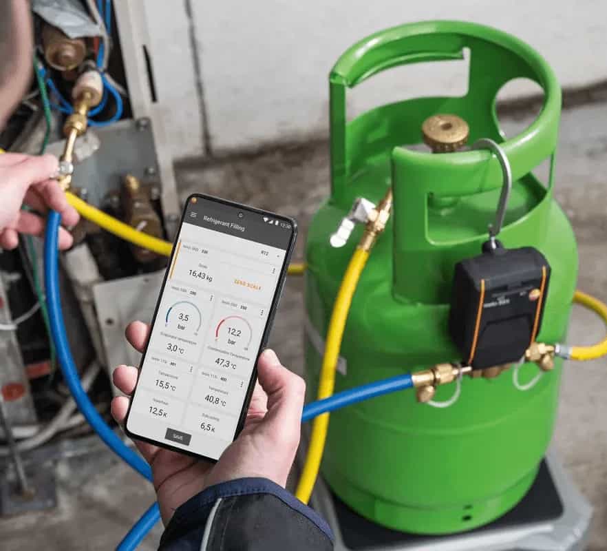 Technik kontroluje napełnianie czynnikiem chłodniczym w aplikacji Testo Smart App na smartfonie obok butli z hosami (miniatura)