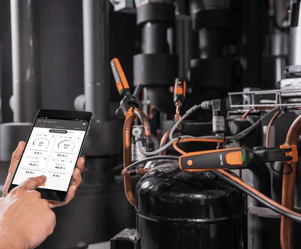 Technik podłączony do jednostki chłodniczej odczytuje wyniki z aplikacji Testo Smart App na tablecie — manometry Testo 549i w użyciu przy sprężarce (miniatura)