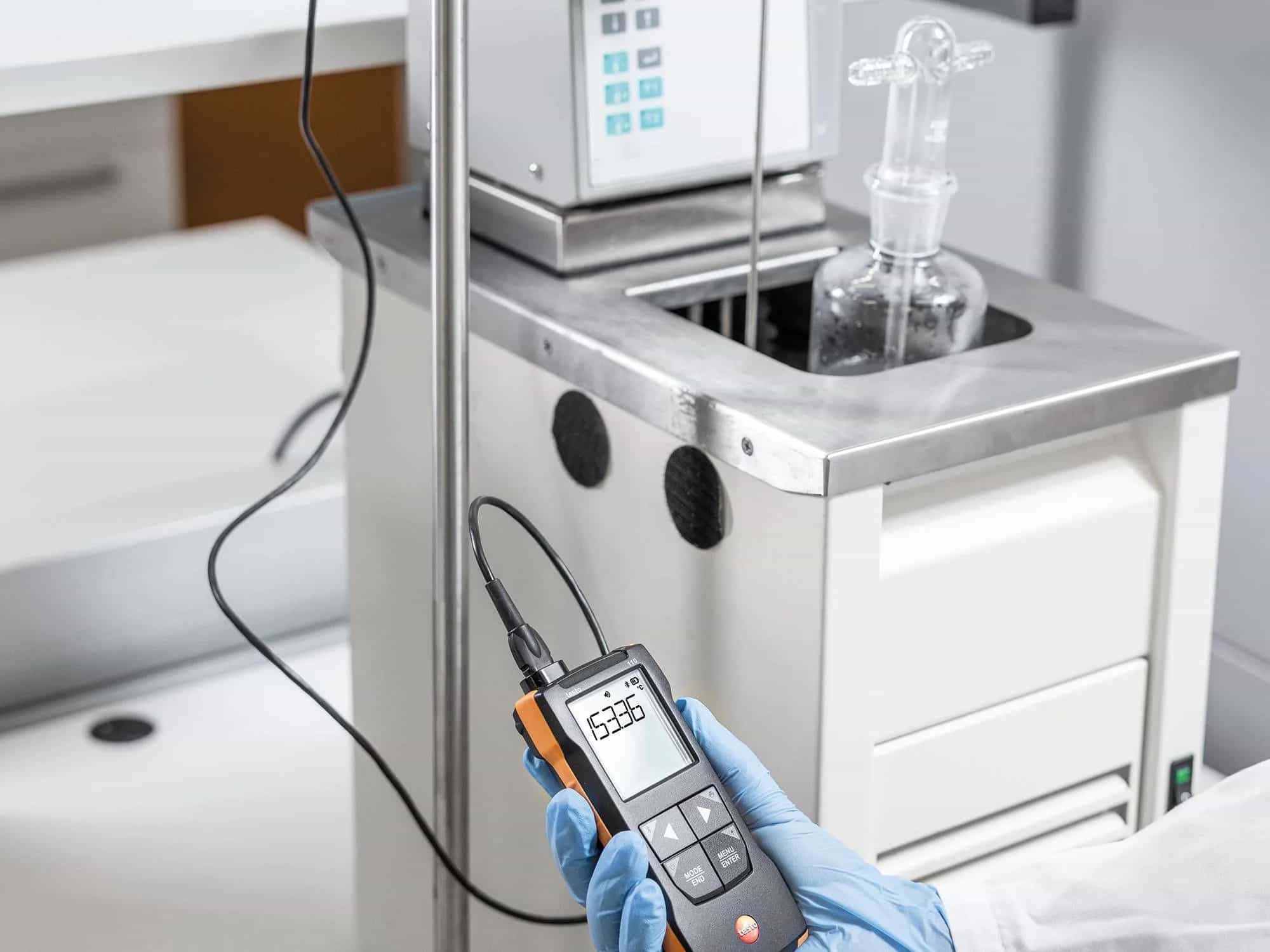 Testo 110 z podłączoną sondą w środowisku laboratoryjnym — użytkownik w rękawiczkach odczytuje wynik pomiaru precyzyjnej łaźni (miniatura)