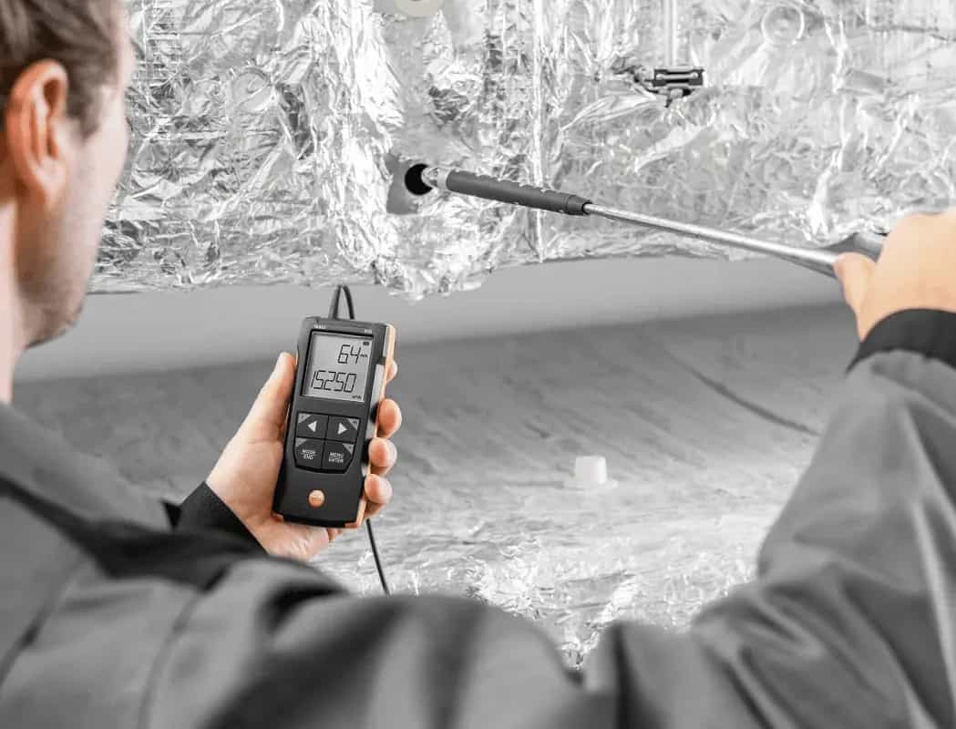 Technik mierzy prędkość przepływu powietrza anemometrem Testo 416 przy kanale wentylacyjnym (miniatura)