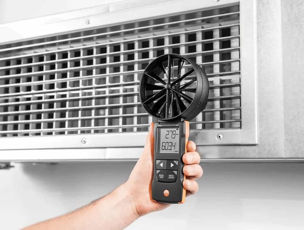 Dłoń przykładająca anemometr wiatraczkowy Testo 417 do kratki nawiewnej podczas pomiaru przepływu powietrza (miniatura)