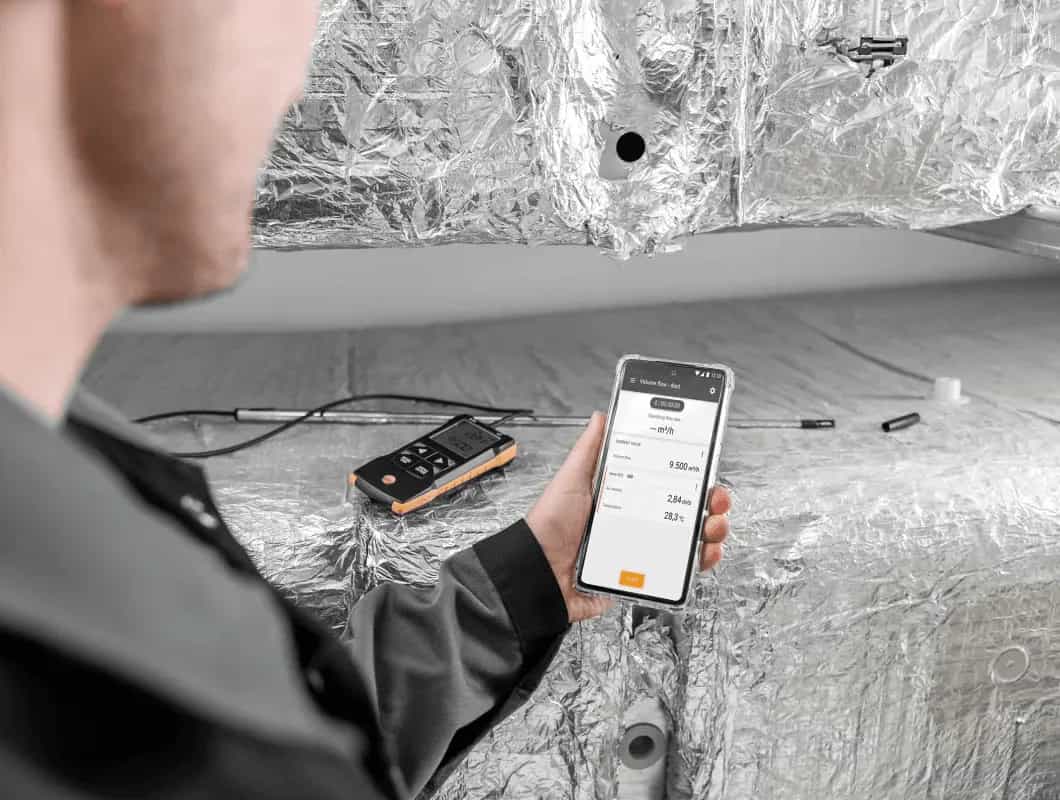 Technik trzymający smartfon z aplikacją Testo Smart App podłączoną do anemometru Testo 425 (miniatura)