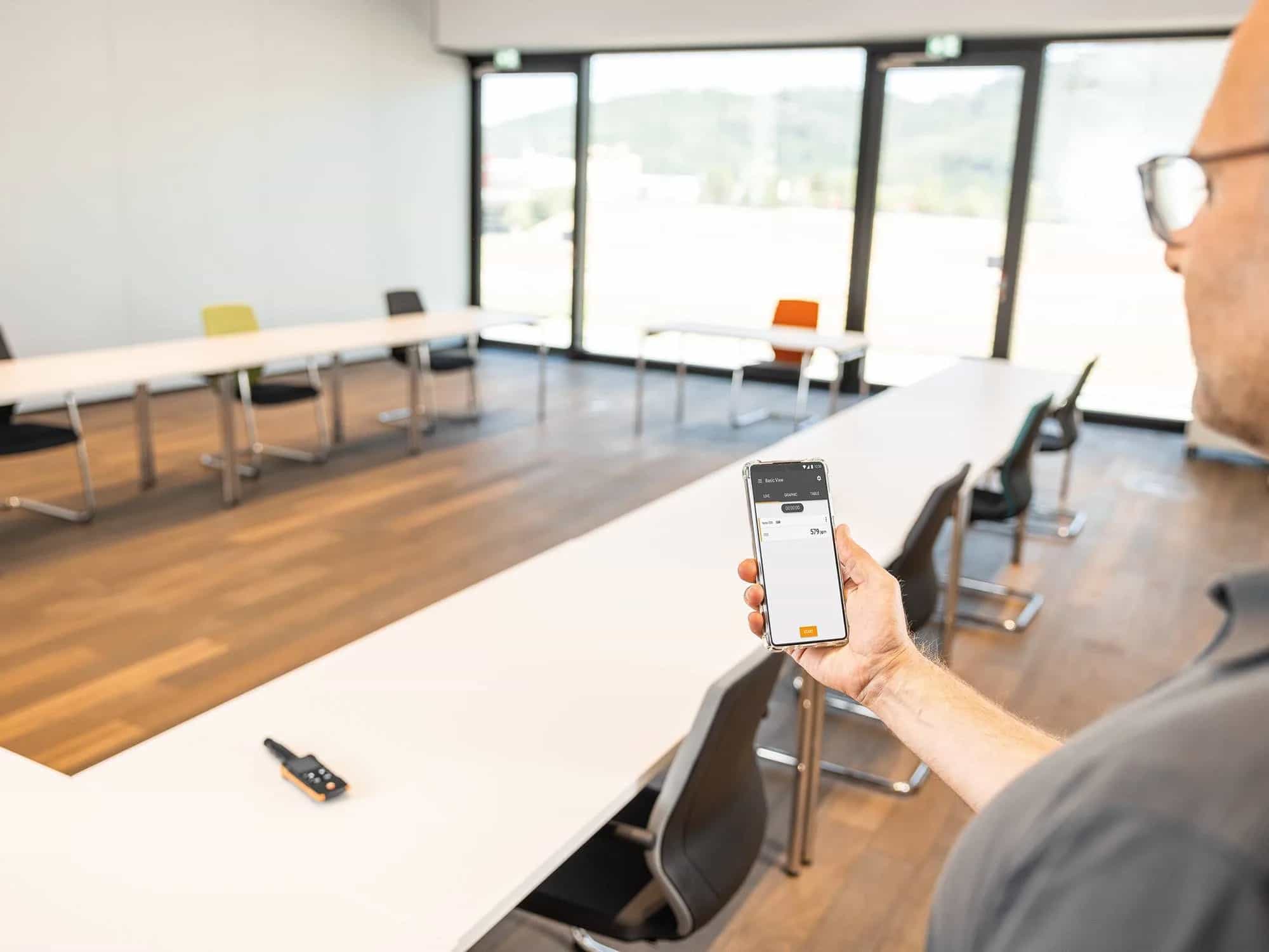 Wyniki pomiaru CO2 z miernika Testo 535 wyświetlane w aplikacji Testo Smart App na smartfonie w sali konferencyjnej (miniatura)