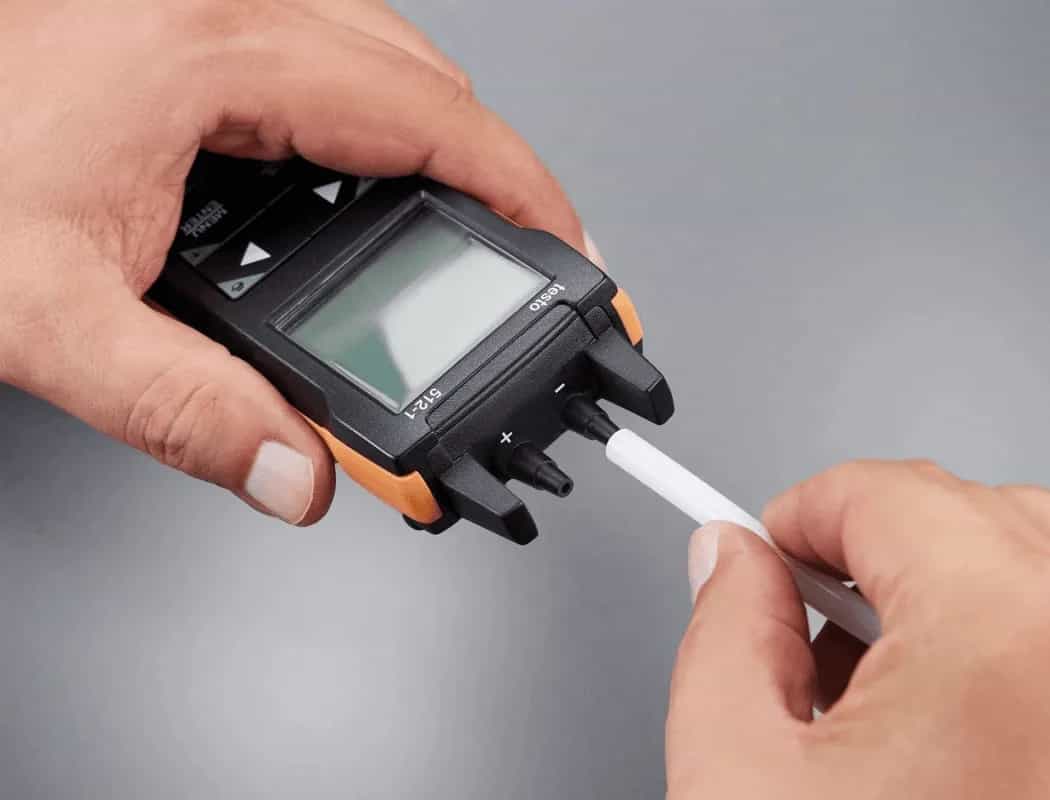 Dłonie podłączają silikonowy wąż do króćca cyfrowego manometru Testo 512-1 (miniatura)