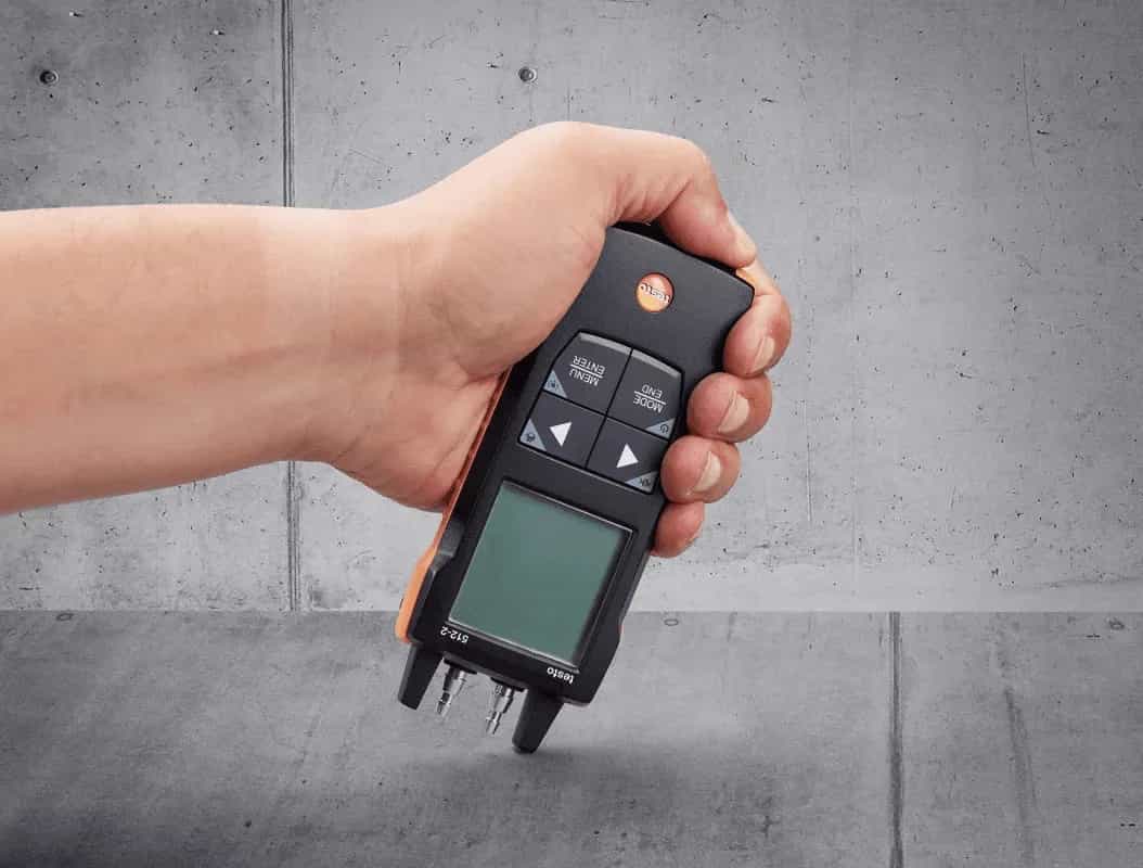 Cyfrowy manometr różnicowy Testo 512-2 trzymany jedną dłonią podczas pomiaru w terenie (miniatura)