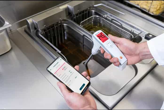 Kucharz trzyma testo 270 BT nad frytkownicą i sprawdza wyniki w aplikacji testo Smart App na telefonie (miniatura)