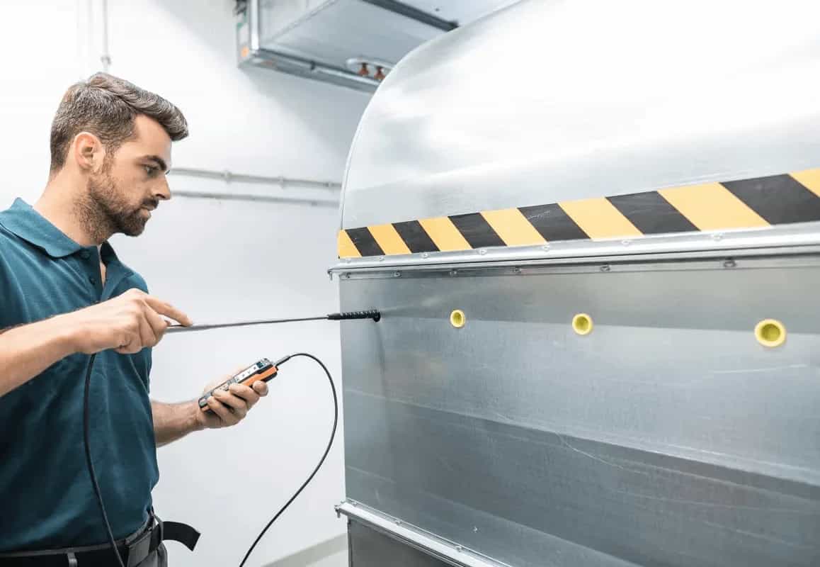 Technik mierzy przepływ powietrza miernikiem Testo 440 przy okapie wyciągowym w pomieszczeniu technicznym (miniatura)