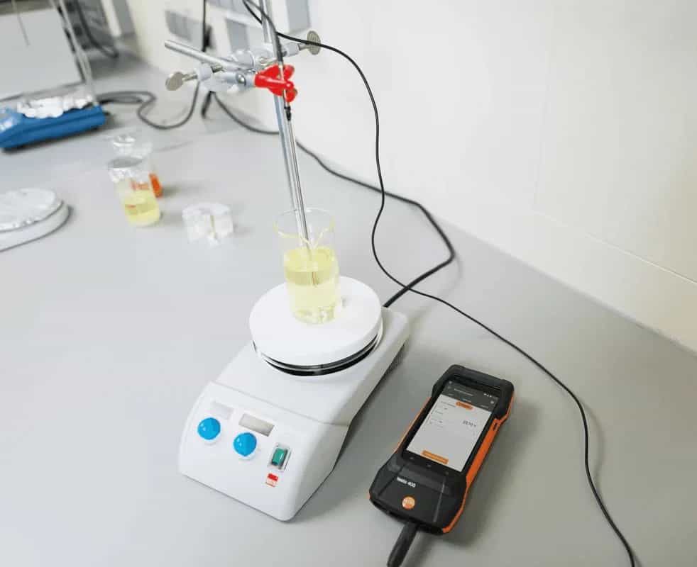 Stanowisko laboratoryjne z sondą Pt100 zanurzoną w zlewce na płycie grzewczej i podłączonym miernikiem Testo 440 na blacie (miniatura)
