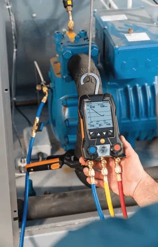 Technik trzymający oprawę zaworową Testo 550s podłączoną do zewnętrznej jednostki agregatu chłodniczego (miniatura)