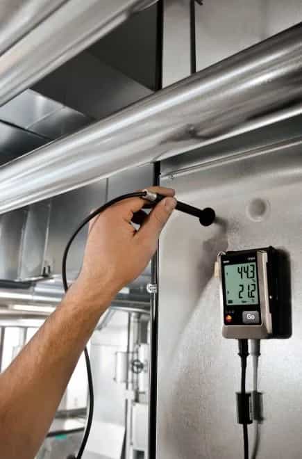 Technik trzymający zewnętrzną sondę przy kanale wentylacyjnym obok zamontowanego rejestratora Testo 176 H1 (miniatura)