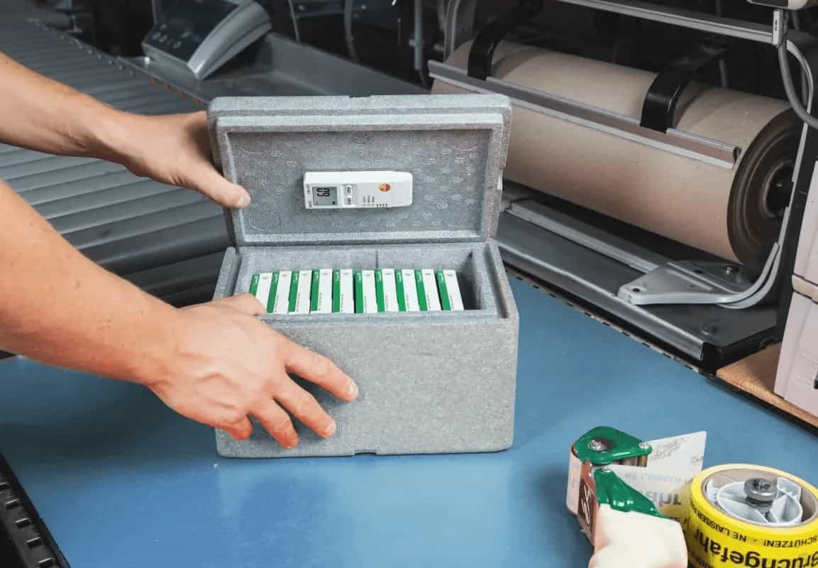 Dłoń umieszczająca rejestrator Testo 184 H1 w izolowanym pojemniku transportowym z chłodzonym ładunkiem w samochodzie dostawczym (miniatura)