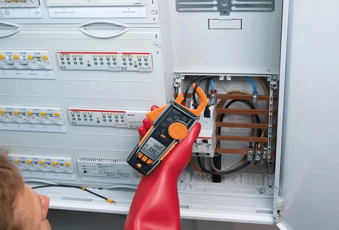 Elektryk w rękawicach ochronnych mierzy prąd amperomierzem cęgowym Testo 770-3 w rozdzielnicy elektrycznej (miniatura)