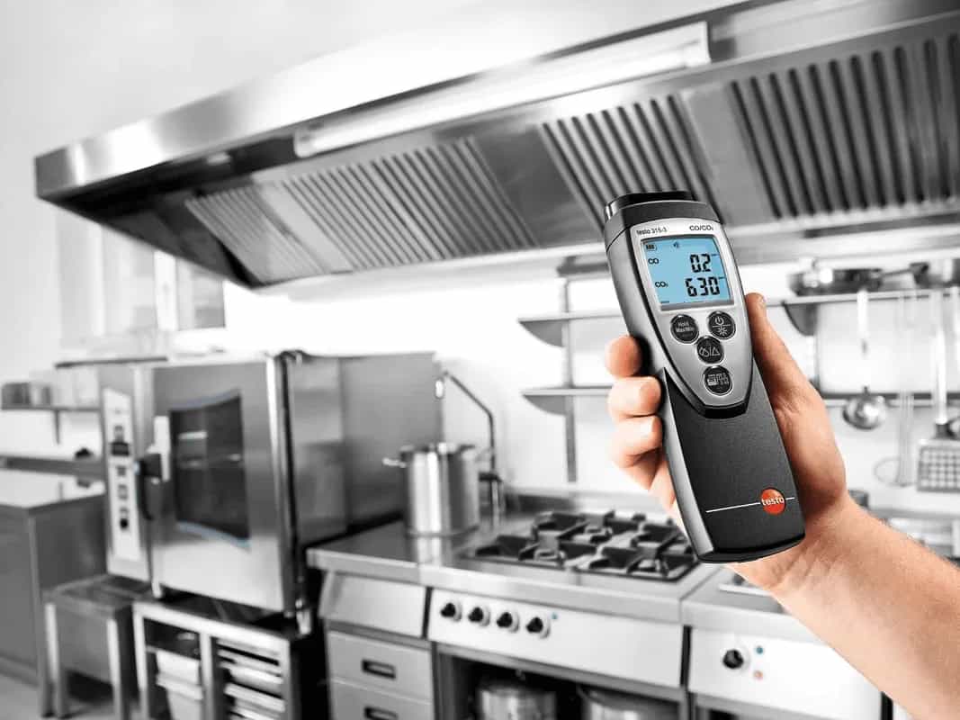 Miernik Testo 315-3 trzymany w dłoni podczas kontroli stężenia CO i CO₂ w kuchni z okapem wentylacyjnym (miniatura)