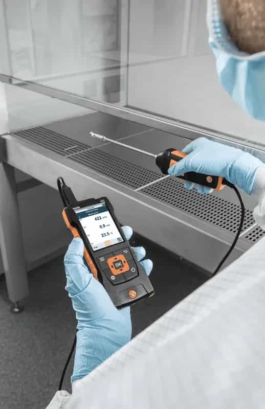 Technik w rękawiczkach mierzący przepływ powietrza w dygestorium laboratoryjnym sondą Testo i miernikiem wielofunkcyjnym (miniatura)
