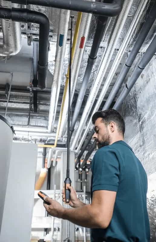 Technik HVAC obsługujący miernik z sondą wiatraczkową Testo w pomieszczeniu technicznym z instalacją wentylacyjną (miniatura)