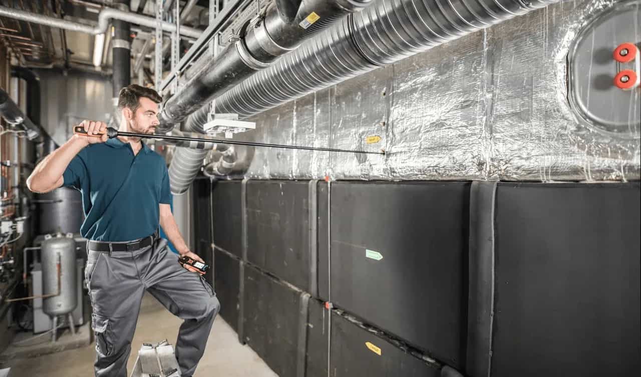Specjalista z sondą wiatraczkową Testo przy dużym systemie wentylacyjnym w pomieszczeniu technicznym (miniatura)