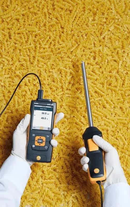 Sonda wilgotności i temperatury Testo 0636 9775 w użyciu — pomiar wilgotności materiałów sypkich (makaronu) trzymana w rękawiczkach ochronnych, obok miernik Testo z wyświetlaczem (miniatura)