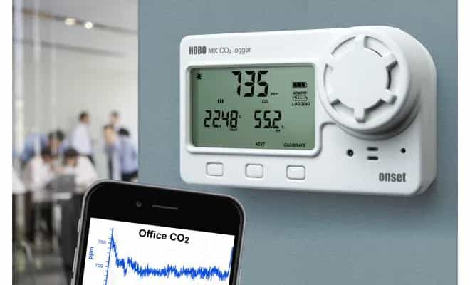 Rejestrator HOBO MX1102A zamontowany na ścianie biura — ekran CO2 i aplikacja HOBOconnect na smartfonie (miniatura)