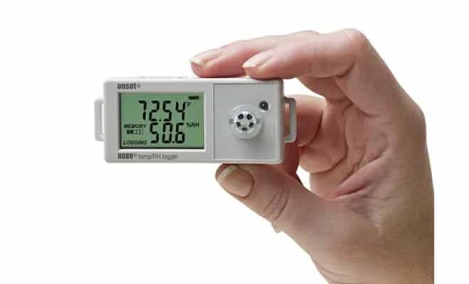 Rejestrator HOBO UX100-011A trzymany w dłoni na tle przestrzeni biurowej podczas monitoringu warunków wewnętrznych (miniatura)