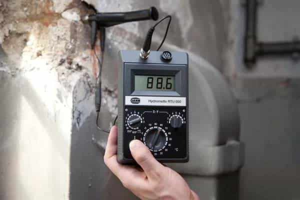 Miernik Gann RTU 600 trzymany w dłoni przy zawilgoconym tynku, z elektrodą przyłożoną do ściany (miniatura)