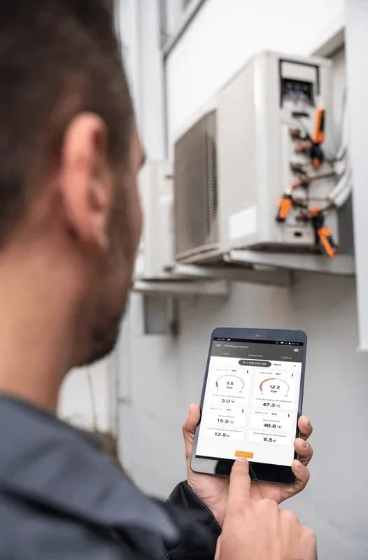 Technik przed zewnętrzną jednostką klimatyzatora odczytuje wyniki na tablecie z aplikacją Testo Smart App
