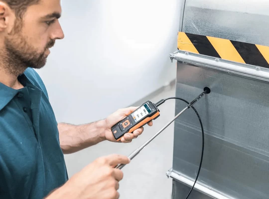 Technik mierzy przepływ i temperaturę powietrza w kanale wentylacyjnym miernikiem Testo 440 z teleskopową sondą na grzany drut