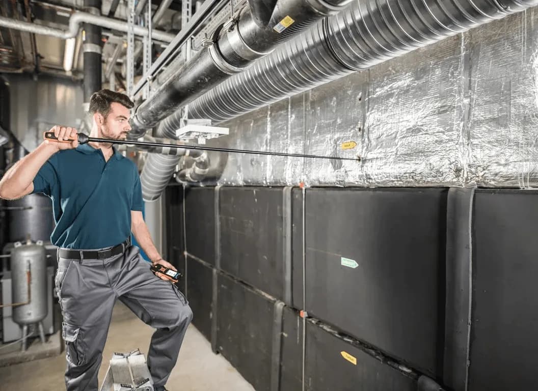 Technik wykonujący pomiar przepływu i temperatury powietrza miernikiem Testo 440 przy instalacji wentylacyjnej w hali technicznej