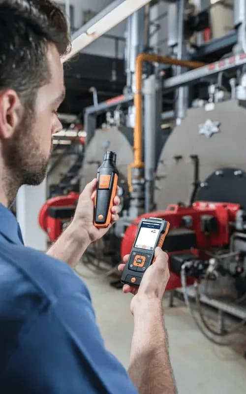 Technik wykonujący pomiar miernikiem Testo w kotłowni z instalacją grzewczą