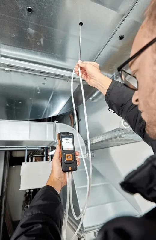 Technik wprowadzający rurkę Pitota do kanału wentylacyjnego podczas pomiaru prędkości przepływu