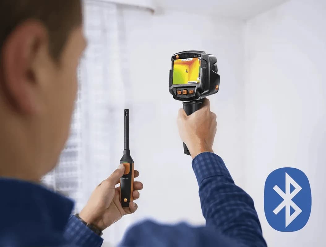 Technik trzymający kamerę termowizyjną Testo 871s i termohigrometr 605i podczas skanowania ściany budynku (miniatura)