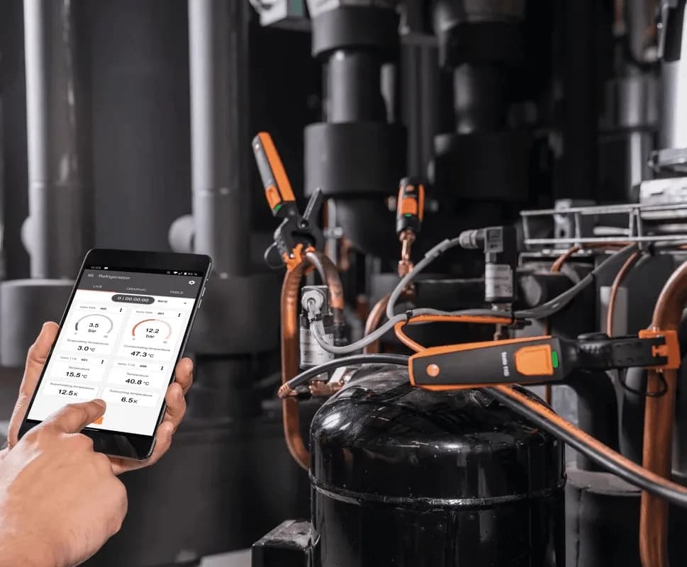 Technik podłączony do jednostki chłodniczej odczytuje wyniki z aplikacji Testo Smart App na tablecie — manometry Testo 549i w użyciu przy sprężarce (miniatura)