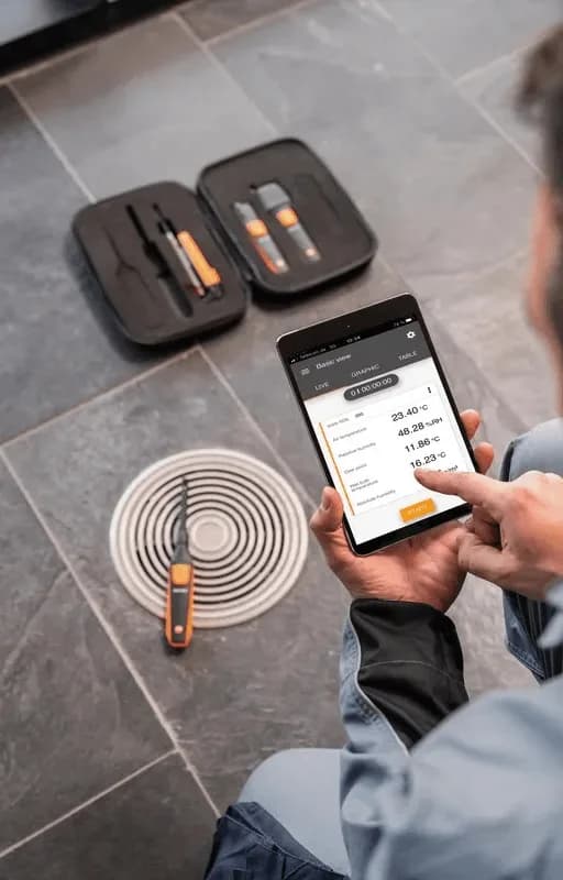 Serwisant mierzący parametry kratki wentylacyjnej miernikiem Testo SmartSond z podglądem wyników w aplikacji Testo Smart App na smartfonie (miniatura)