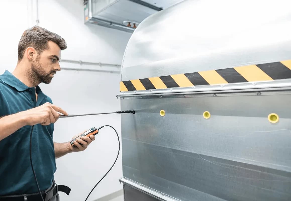 Technik mierzy przepływ powietrza miernikiem Testo 440 przy okapie wyciągowym w pomieszczeniu technicznym (miniatura)