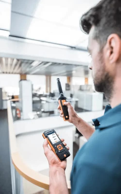 Technik trzymający miernik Testo z podłączoną sondą CO₂ Bluetooth, odczytujący wyniki na smartfonie w hali (miniatura)