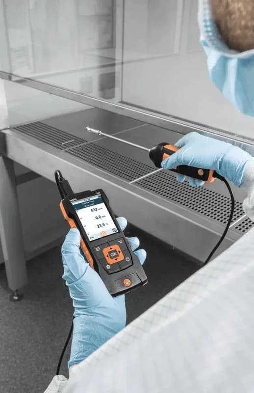 Technik w rękawiczkach mierzący przepływ powietrza w dygestorium laboratoryjnym sondą Testo i miernikiem wielofunkcyjnym (miniatura)
