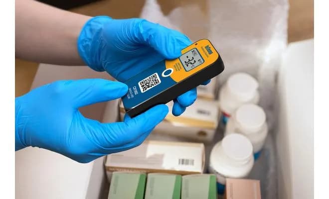 Pracownik w niebieskich rękawiczkach trzymający rejestrator Onset CX1003 przy paczkach farmaceutycznych w pudełku transportowym (miniatura)