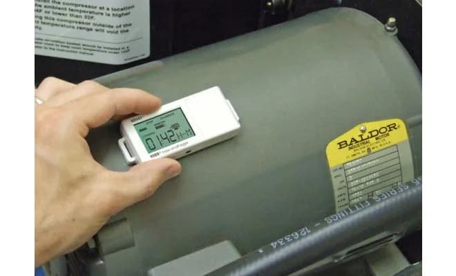 Rejestrator HOBO UX90-004 przyłożony ręką do obudowy silnika elektrycznego w hali przemysłowej (miniatura)