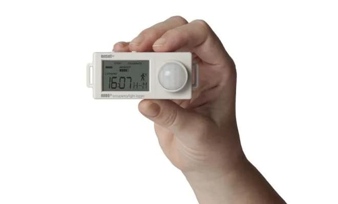 Rejestrator HOBO UX90-006 trzymany w dłoni na tle sali konferencyjnej z oświetleniem LED (miniatura)