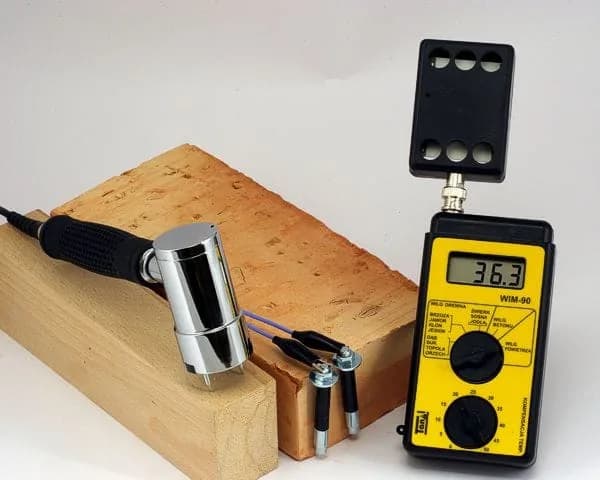 Elektroda młotkowa WIM-90 przy próbce drewna podczas pomiaru wilgotności — widok elektrod wbitych w materiał (miniatura)