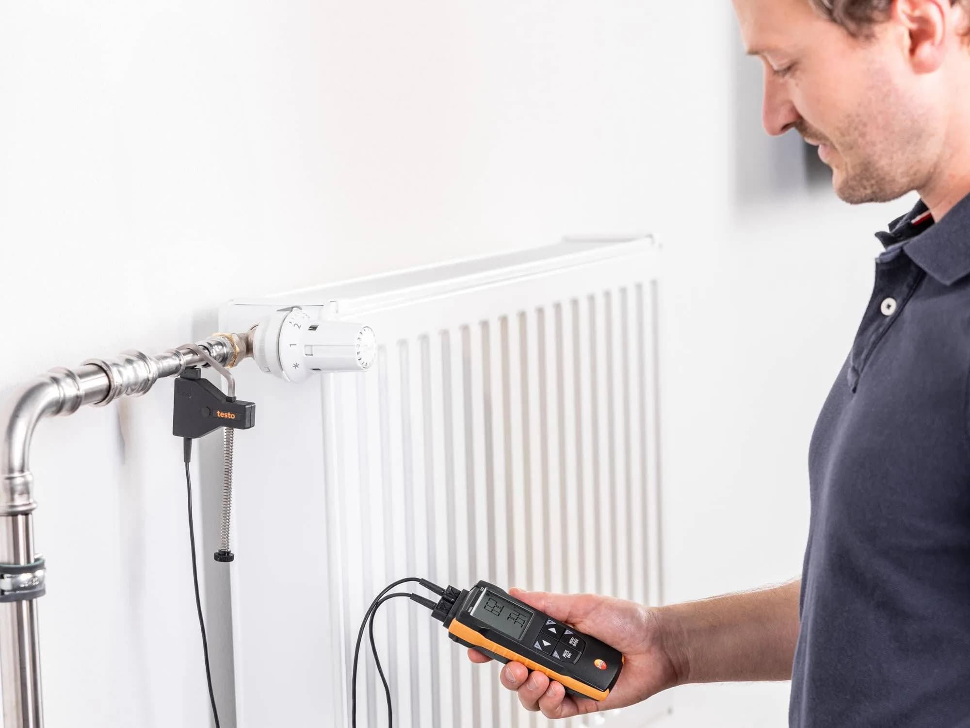 Technik serwisowy odczytuje wynik pomiaru różnicy temperatur na termometrze Testo 922 przy instalacji grzewczej z grzejnikiem
