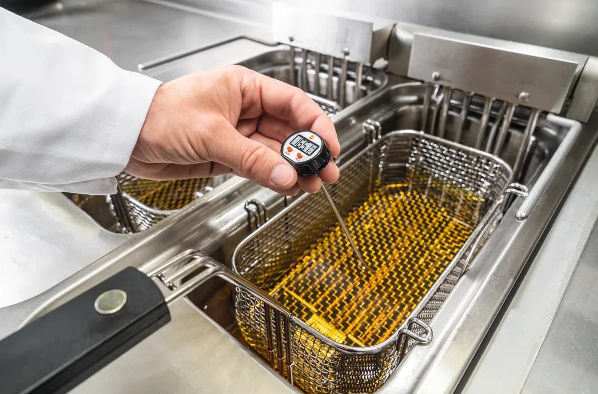 Kucharz mierzy termometrem temperaturę oleju we frytownicy gastronomicznej, odczyt 165 °C