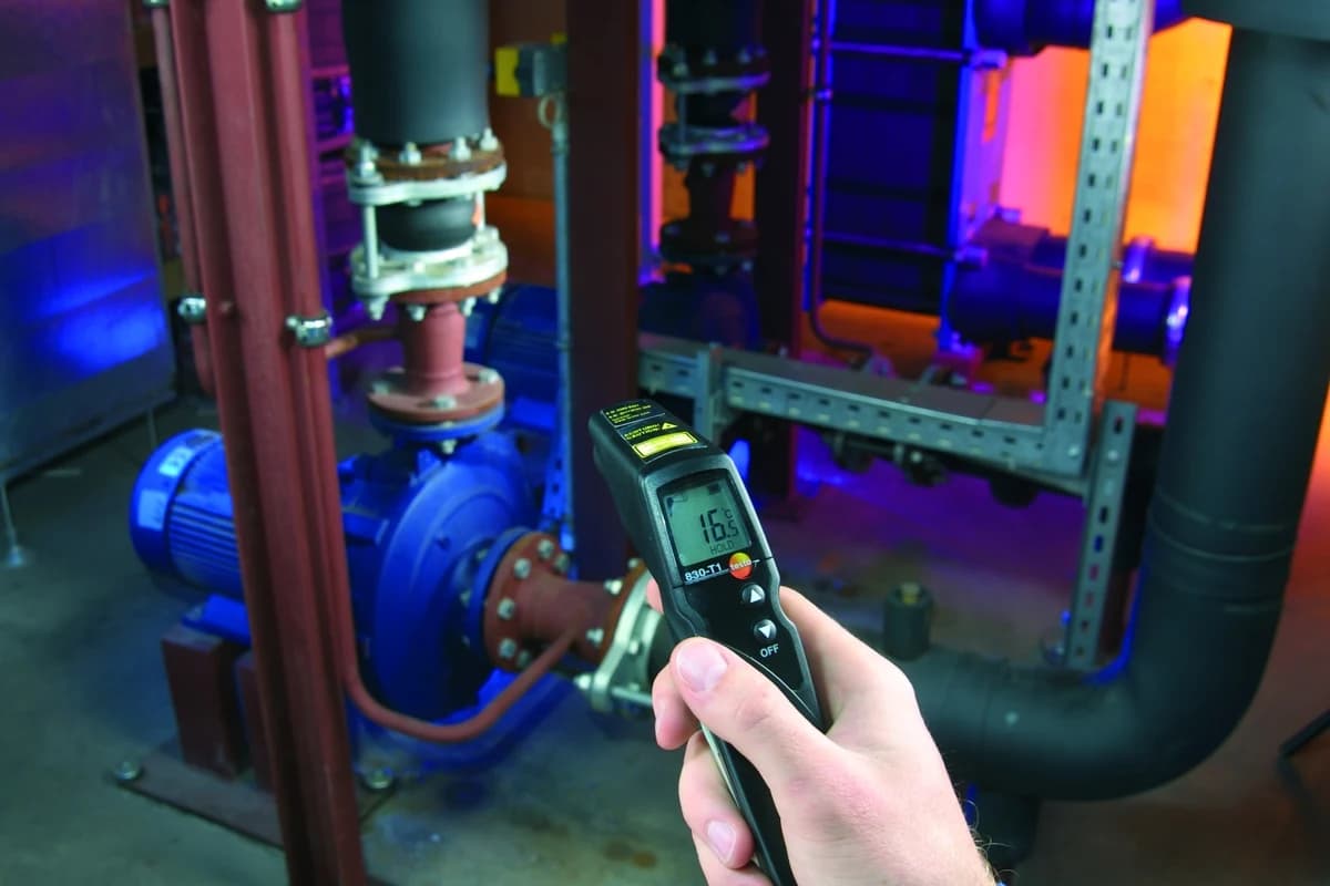 Pirometr Testo 830-T1 wycelowany w korpus pompy w instalacji technicznej, z zatrzymanym odczytem na wyświetlaczu